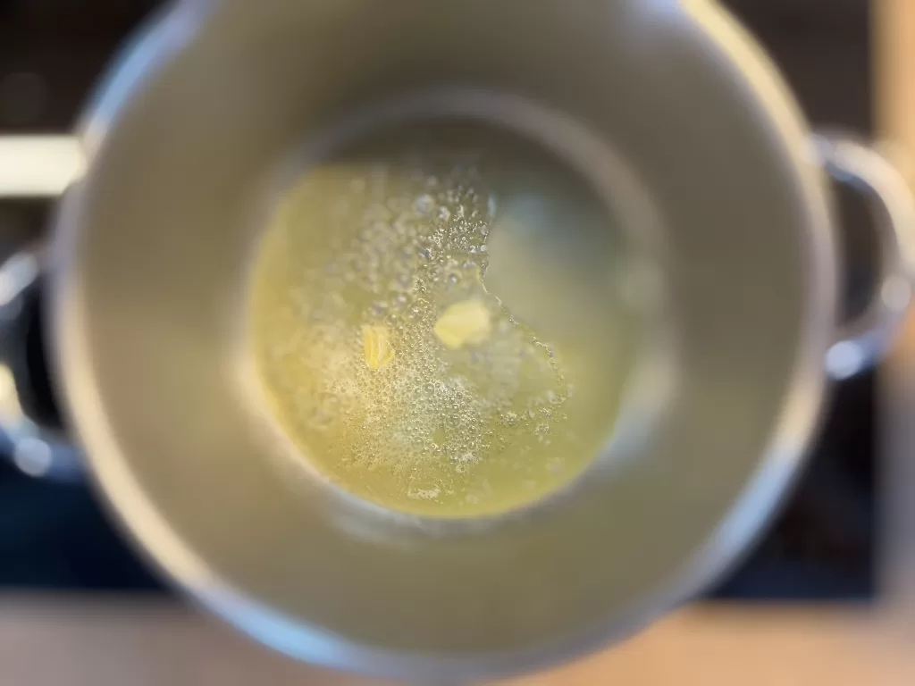 Obrázek přípravy polévky: V hrnci rozpálíme máslo s trochou olivového oleje